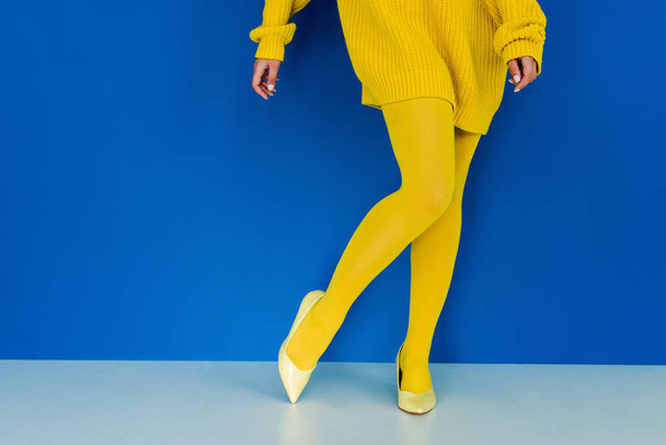 黄色い服と青の背景にポーズの靴を身に着けている女性のビューをトリミング - 写真・画像