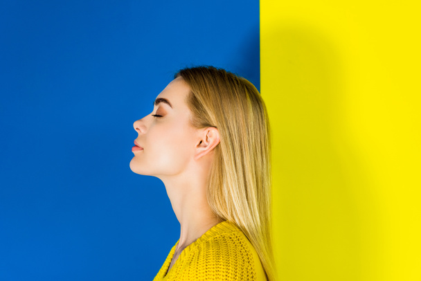 Πορτρέτο του ξανθού κοριτσιού με κλειστά τα μάτια σε μπλε και κίτρινο φόντο - Φωτογραφία, εικόνα