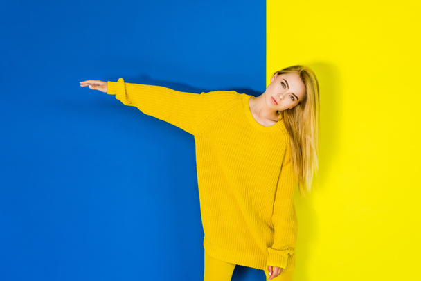 Attractive young girl posing in yellow clothes on blue and yellow background - Photo, Image