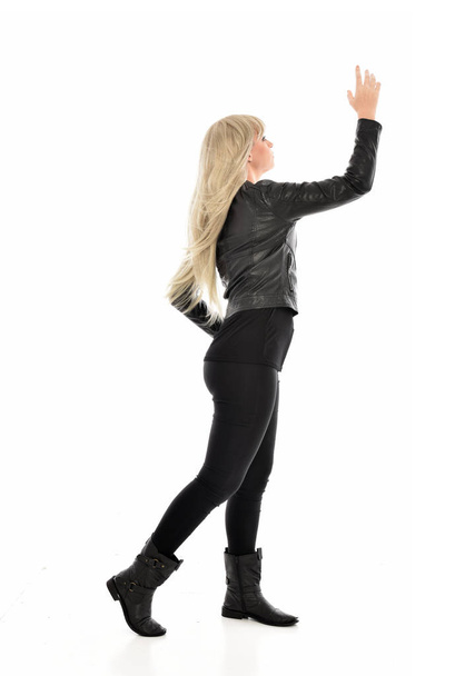 full length portrait of blonde girl wearing black leather clothes. standing pose with back to the camera. isolated on white studio background. - Fotó, kép