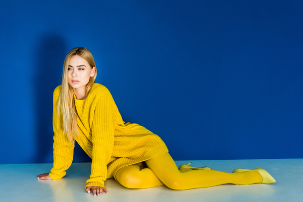 Jovem sedutora em roupas de moda amarela deitada no fundo azul
 - Foto, Imagem