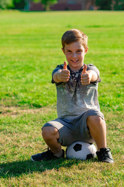 Happy pre-teen boy sitting on a football. Won a match concept - Fotografie, Obrázek