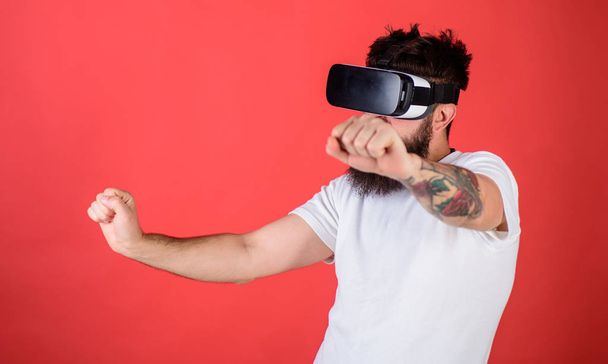 Virtual racing concept. Man with beard in VR glasses driving motorbike, red background. Hipster on confident face driving bike on high speed in virtual reality. Guy play racing game in VR - Foto, Imagem