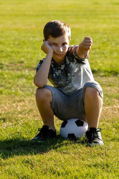 Unhappy boy sitting on a football. Lost a game concept - Foto, imagen