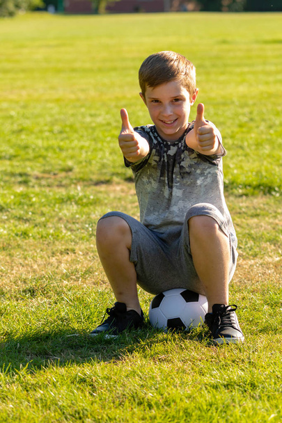 Happy pre-teen boy sitting on a football. Won a match concept - Zdjęcie, obraz