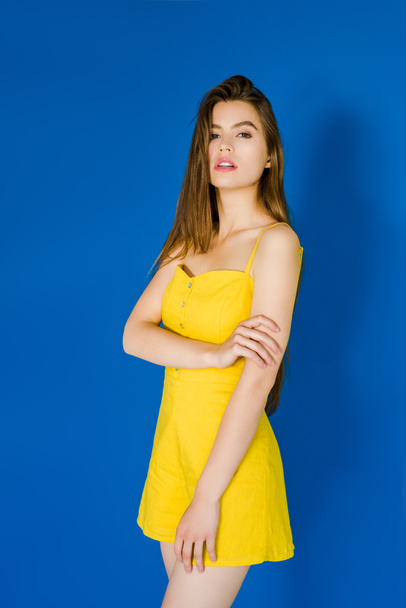 Elegant brunette woman in yellow dress posing on blue background - 写真・画像