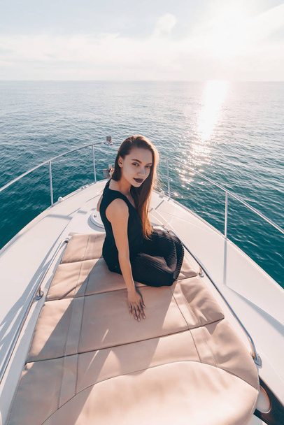 lovely long-haired girl in black clothes is resting on a yacht, posing, sailing on the Caribbean sea - Zdjęcie, obraz