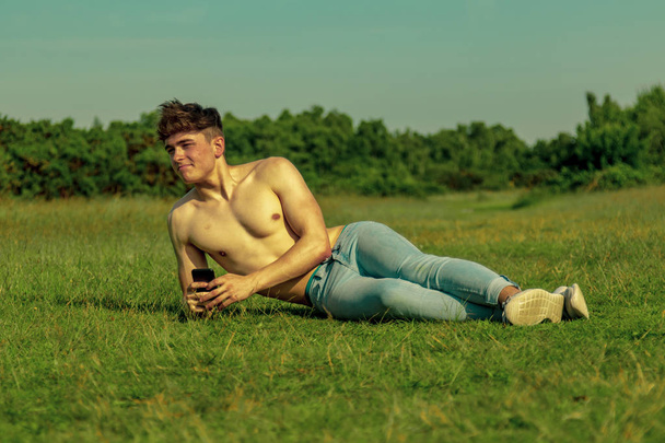 Shirtless young male dult using a mobile phone on a warm summer's day - Photo, Image