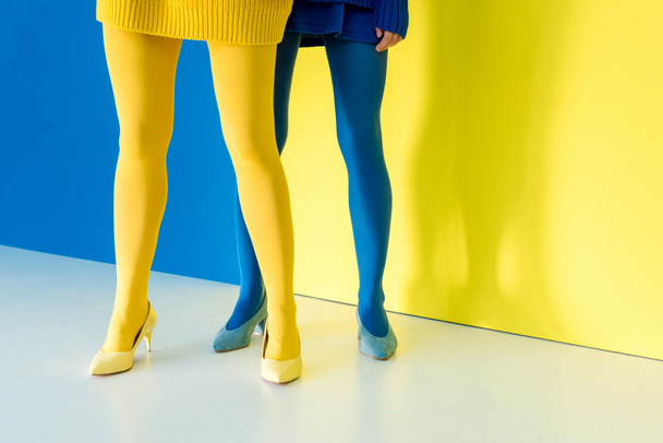 Cropped view of female legs in blue and yellow pantyhose on blue and yellow background - Foto, imagen