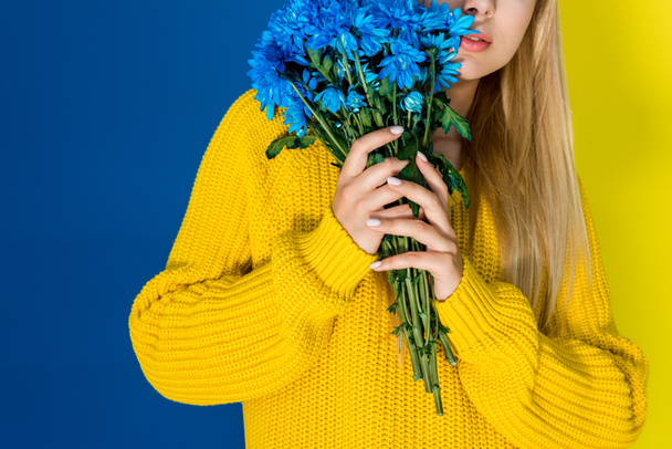 Girl in yellow sweater holding blue flowers isolated on blue and yellow background - Foto, Bild