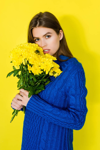 Beautiful brunette girl holding bouquet of yellow chrysanthemums on yellow background - Valokuva, kuva