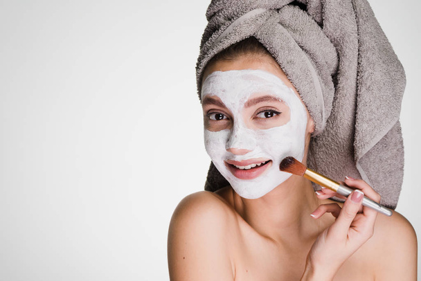 lovely young girl with a towel on her head puts a useful white mask on her face, smiling - Foto, Bild