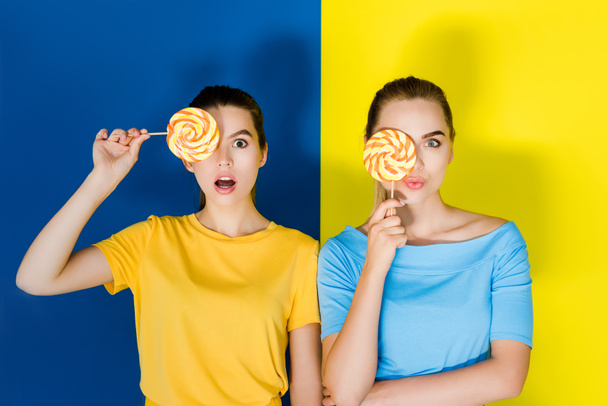 Female fashion models holding lollipops on blue and yellow background - Foto, imagen