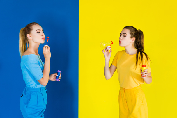 schöne brünette und blonde Mädchen blasen Blasen auf blauem und gelbem Hintergrund - Foto, Bild