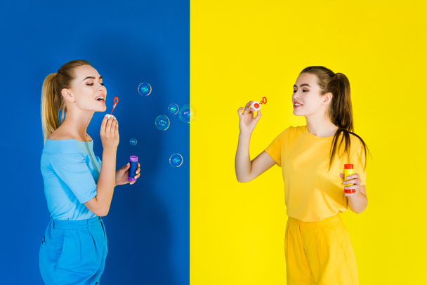 Elegant stylish women blowing bubbles on blue and yellow background - Foto, afbeelding