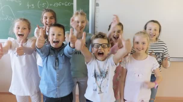 Niños de pie cerca de la junta escolar y mostrando los pulgares hacia arriba y sonriendo
 - Imágenes, Vídeo