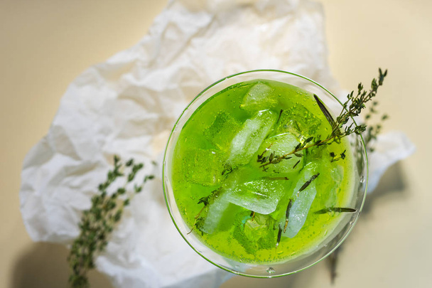 Зеленый напиток с кубиками льда и зелеными ветвями в стакане для мохито на мятой оберточной бумаге на желтом столе. Концептуальный и рекламный дизайн. Копирование пространства
. - Фото, изображение