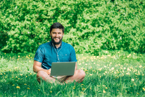 Young businessman or student in casual dress using laptop in the park. Outdoor office concept - Fotó, kép