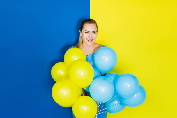 Female fashion model holding party balloons on blue and yellow background - Photo, Image