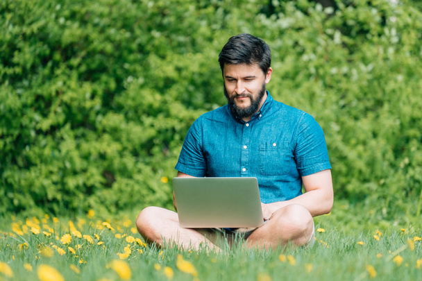 Happy cheerful hipster man with a laptop sitting outdoors on green grass. Freedom  concept - Foto, Imagem
