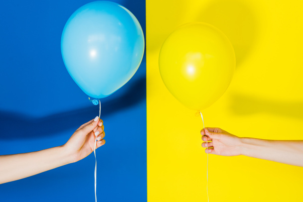 Περικοπεί άποψη των γυναικών χέρια με μπαλόνια σε μπλε και κίτρινο φόντο - Φωτογραφία, εικόνα