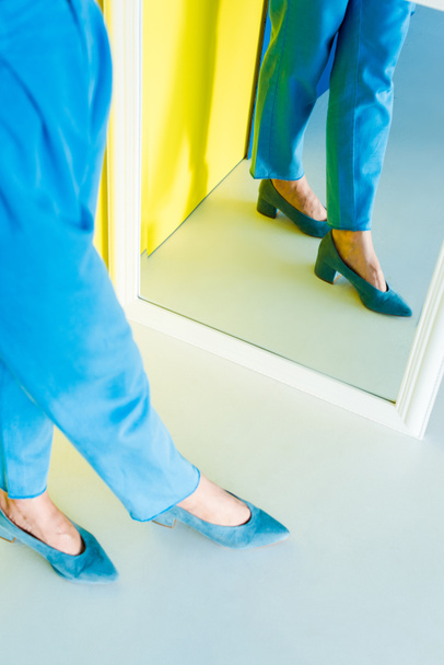 Oříznuté mirror pohled ženy v modrém oblečení a boty na modré a žluté pozadí - Fotografie, Obrázek