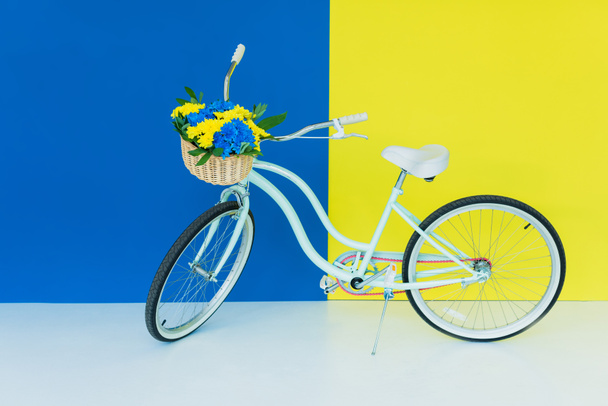 Female bicycle with flowers in basket on blue and yellow background - Photo, Image