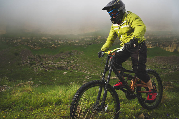 Un hombre en un casco de montaña montando una bicicleta de montaña pasea por la hermosa naturaleza en un clima nublado. cuesta abajo
 - Foto, imagen
