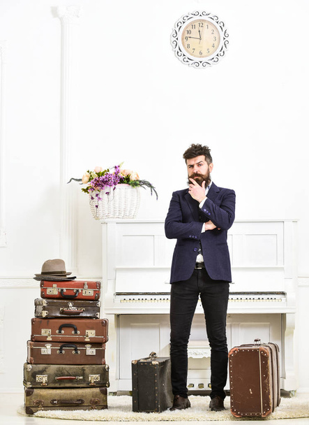 Macho elegant on thoughtful face standing near pile of vintage suitcase. Luggage and travelling concept. Man, traveller with beard and mustache with luggage, luxury white interior background - Foto, Imagem