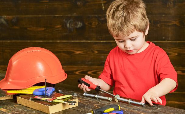 Toddler on busy face plays with screwdriver tool at home in workshop. Childhood concept. Child cute and adorable playing as builder or repairer, repairing or handcrafting. Kid boy play as handyman - Fotoğraf, Görsel
