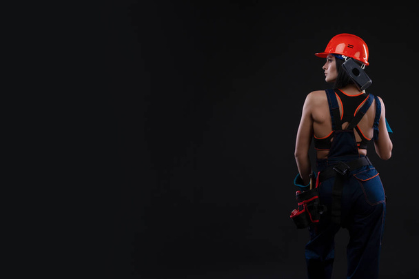 Rückansicht einer Arbeiterin mit Hammer und Helm auf schwarzem Hintergrund. . Gleichstellung der Geschlechter. Kopierraum - Foto, Bild