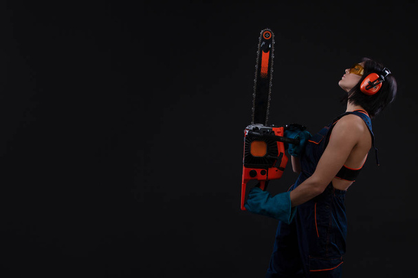 young woman with motor saw or chainsaw on a black background. gender equality. Copy space - Фото, зображення