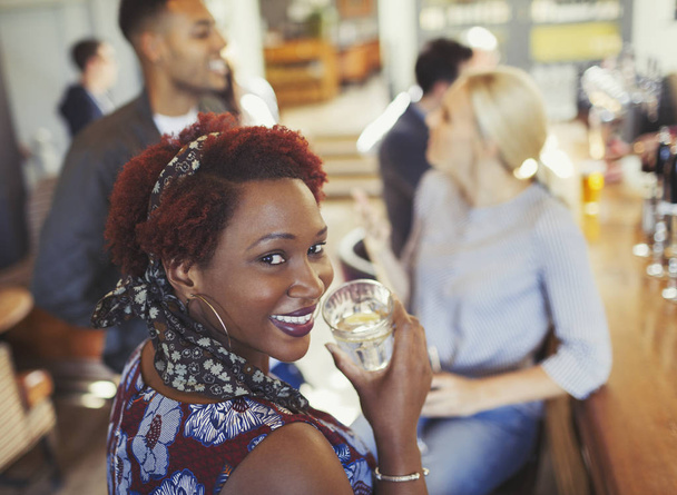 Portret lachende vrouw drinkwater en praten met vrienden bij bar - Foto, afbeelding