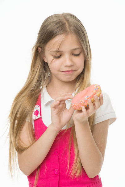 Girl with long blond hair holding yummy desert. Kid picking colorful sprinkles off doughnut. Sweet tooth in pink outfit isolated on white background. Girl eating icing from bagel, sugar coma concept - Foto, Bild