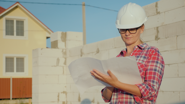 A female engineer is studying a drawing. It stands on the construction site of a small cottage - Footage, Video