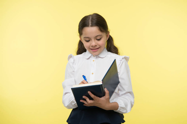 Schoolgirl write in notebook on yellow background. Girl in school uniform, back to school. Little child with writing pad. Fashion genius. Creating my future - Fotoğraf, Görsel