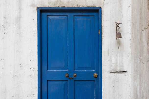 Puerta de madera azul icónico antiguo con pared blanca sucia, campana, y decoración de lagarto falso
. - Foto, Imagen