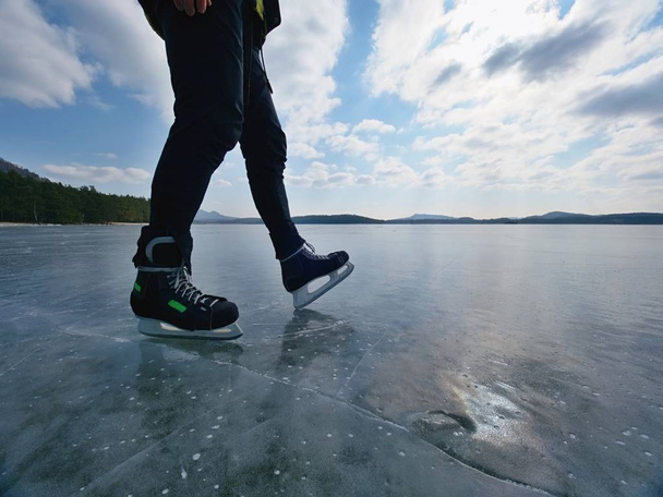 Man ice skating on frozen lake. Thin ice with deeep cracks below man legs. - Photo, Image
