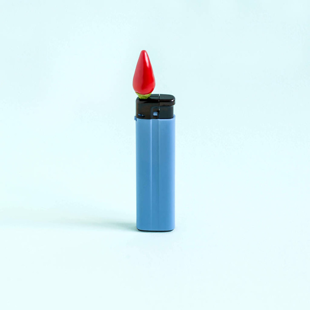 Αερίου αναπτήρα με καυτερή πιπεριά αντί για φωτιά σε παστέλ μπλε φόντο. Μινιμαλιστικό στυλ, φαντασία και φαντασία. Δημιουργική ιδέα της καύσης μπαχαρικά - Φωτογραφία, εικόνα