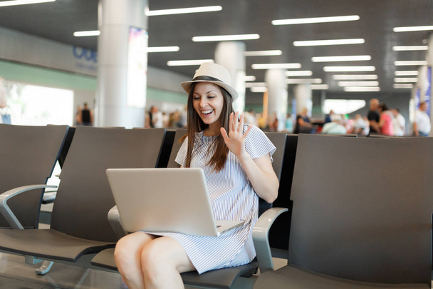 Fiatal utazók turisztikai nő dolgozik laptop, a hullám kéz Üdvözlés web-kamera közben video hív vár a lobbi csarnokában airport. Személyszállítás külföldre utazik a hétvégi kiruccanás. Légi járat koncepció - Fotó, kép