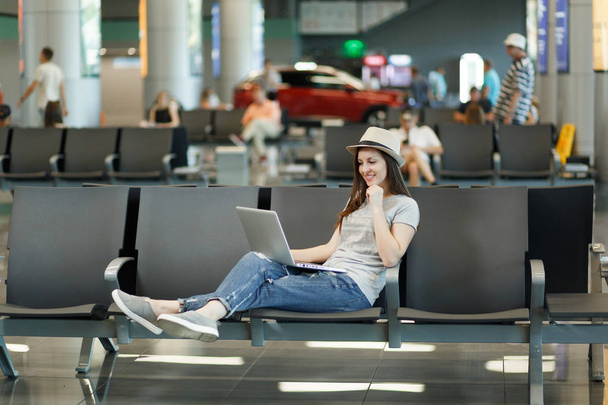 若い思考旅行観光女性国際空港でホールはロビーで待っている間のラップトップに取り組んでの帽子。週末休暇に海外旅行の乗客。空気旅行は、フライトの旅のコンセプト - 写真・画像
