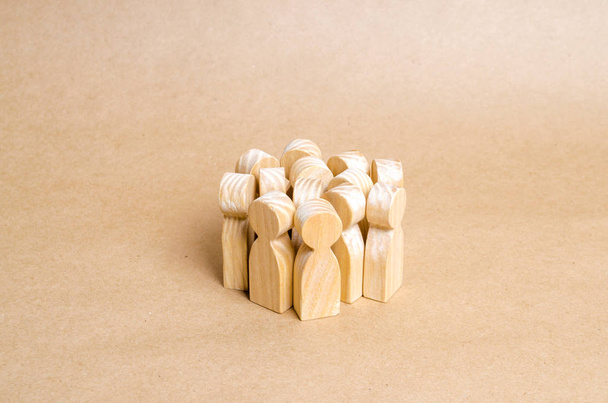 A crowd of wooden figures of people stands in a pile on a beige paper background. The concept of cohesion and cooperation. Frightened people, herd behavior. Team, target audience - Foto, Imagem
