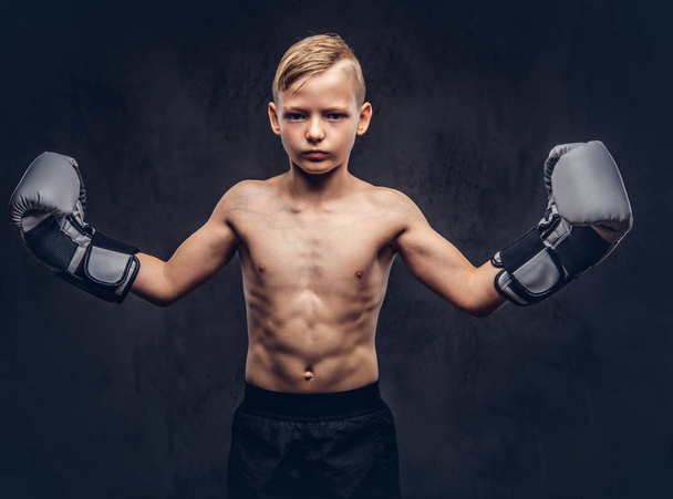 Молодой боксёр без рубашки в боксёрских перчатках позирует в студии. Изолированный на темном текстурированном фоне
. - Фото, изображение
