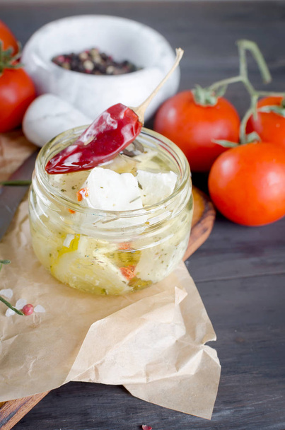 Marinated spicy  feta in a jar, tomatoes for salad. On a dark background. Copy space for your text.  - Zdjęcie, obraz