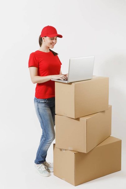 Ολόσωμο Πορτρέτο γυναίκας παράδοσης στο κόκκινο καπάκι, t-shirt που απομονώνονται σε λευκό φόντο. Θηλυκό courier στέκεται κοντά άδειο χαρτοκιβώτια με φορητό υπολογιστή pc. Λήψη το πακέτο. Χώρο αντίγραφο - Φωτογραφία, εικόνα