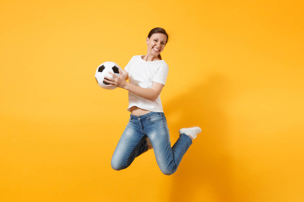 Νέοι διασκέδαση εκφραστική Ευρωπαία γυναίκα ποδόσφαιρο ανεμιστήρα άλμα στον αέρα, να φτιάξει ομάδα υποστήριξης, κρατώντας την μπάλα ποδοσφαίρου που απομονώνονται σε κίτρινο φόντο. Παίξτε ποδόσφαιρο, ευθυμία, άθλημα, ανεμιστήρες άτομα lifestyle έννοια - Φωτογραφία, εικόνα