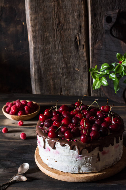 Chocolate cake with whipped cream on wooden desk and wooden background. Cherry cake with chocolate. Raspberry in wooden plate. Rustic foodphotography. Still life food. - Foto, Bild