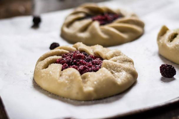 Raw summer galette with berries, raspberry, blueberry, blackberry, apple and crusty sugar vegetarian dough. Summer food, summer pie on parchment paper. Preparation, cooking food, raw dough. Apple pie. - Photo, Image