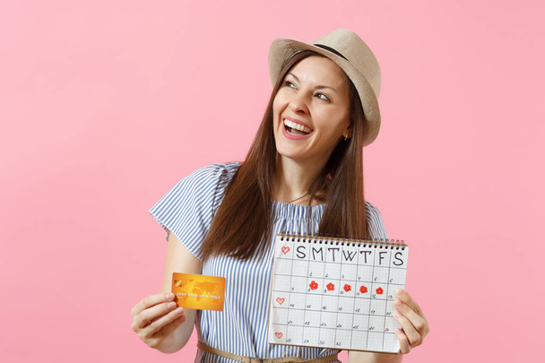 Portret van gelukkige vrouw in blauwe jurk, hoed bedrijf creditcard, periodes kalender, controle menstruatie dagen geïsoleerd op trending roze achtergrond. Medische gezondheidszorg gynaecologische concept. Kopiëren van ruimte - Foto, afbeelding