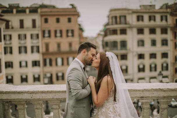 Young attractive newly married couple walking and posing in Rome with beautiful and ancient architecture on the background on their wedding day - Fotografie, Obrázek